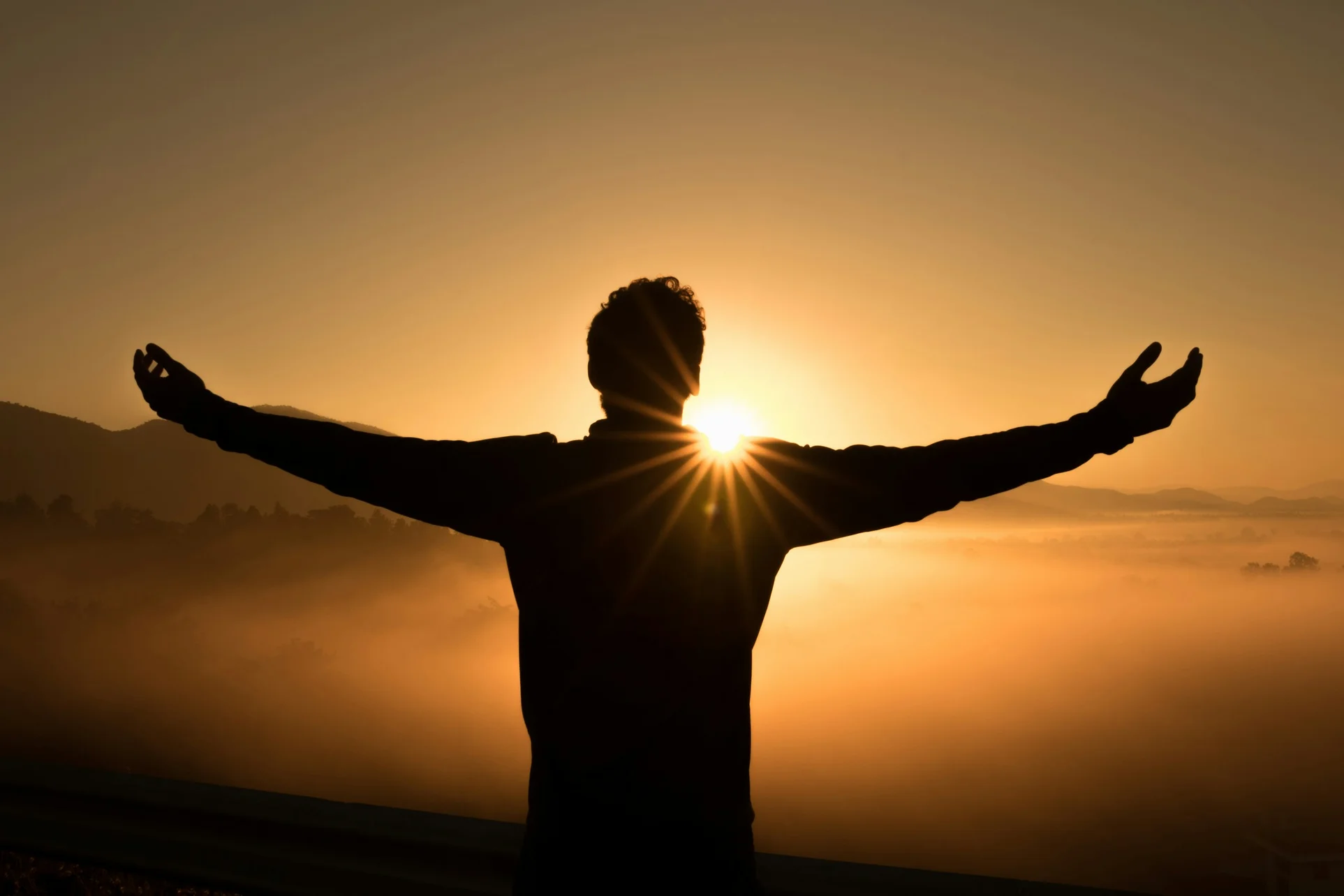 Un hombre observa el sol con los brazos abiertos.